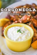 A straight-on view of a small yellow bowl that is filled with a gorgonzola dipping sauce and is sitting on a platter next to a pile of cooked wings.
