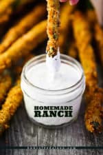The tip of a fried asparagus being dipped into a small jar of homemade ranch dressing.
