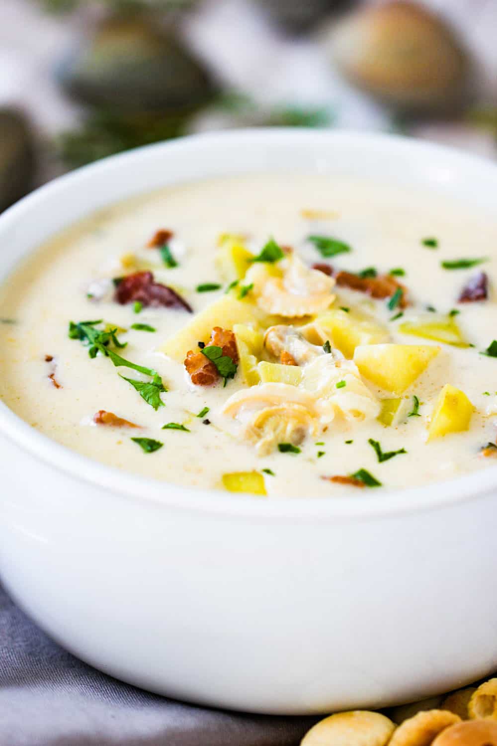 A close up view of a white bowl of New England Clam Chowder with fresh clams next to it.