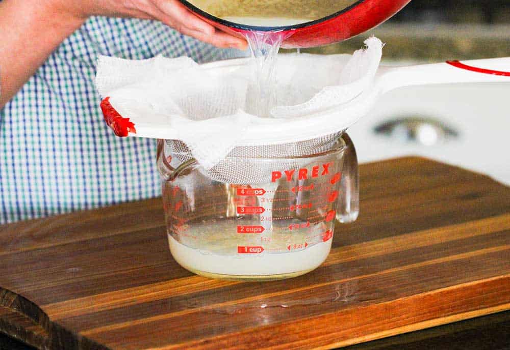 Two hands straining clam juice through cheesecloth over a measuring cup.