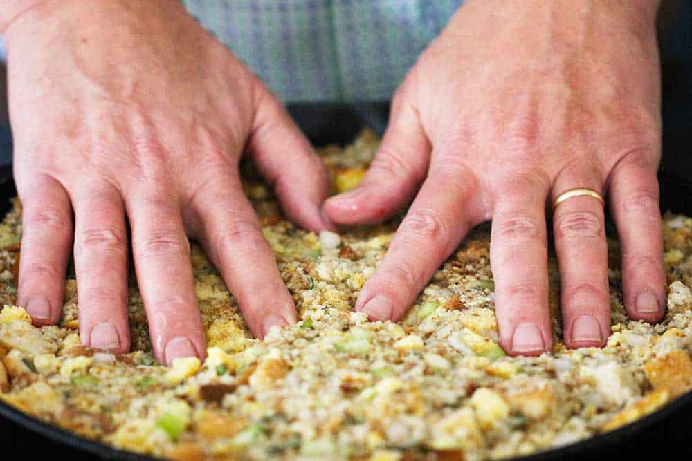 Two hands pressing onto a pan full of Thanksgiving dressing. 