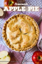 An overhead view of a homemade apple pie next to cut apples on a checkered place mat.