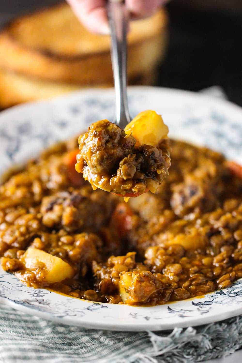 A hand holding a spoon of lentil soup over a bowl of the soup. 