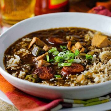A white bowl chicken and sausage gumbo on top of patterned napkin with a spoon next to it.