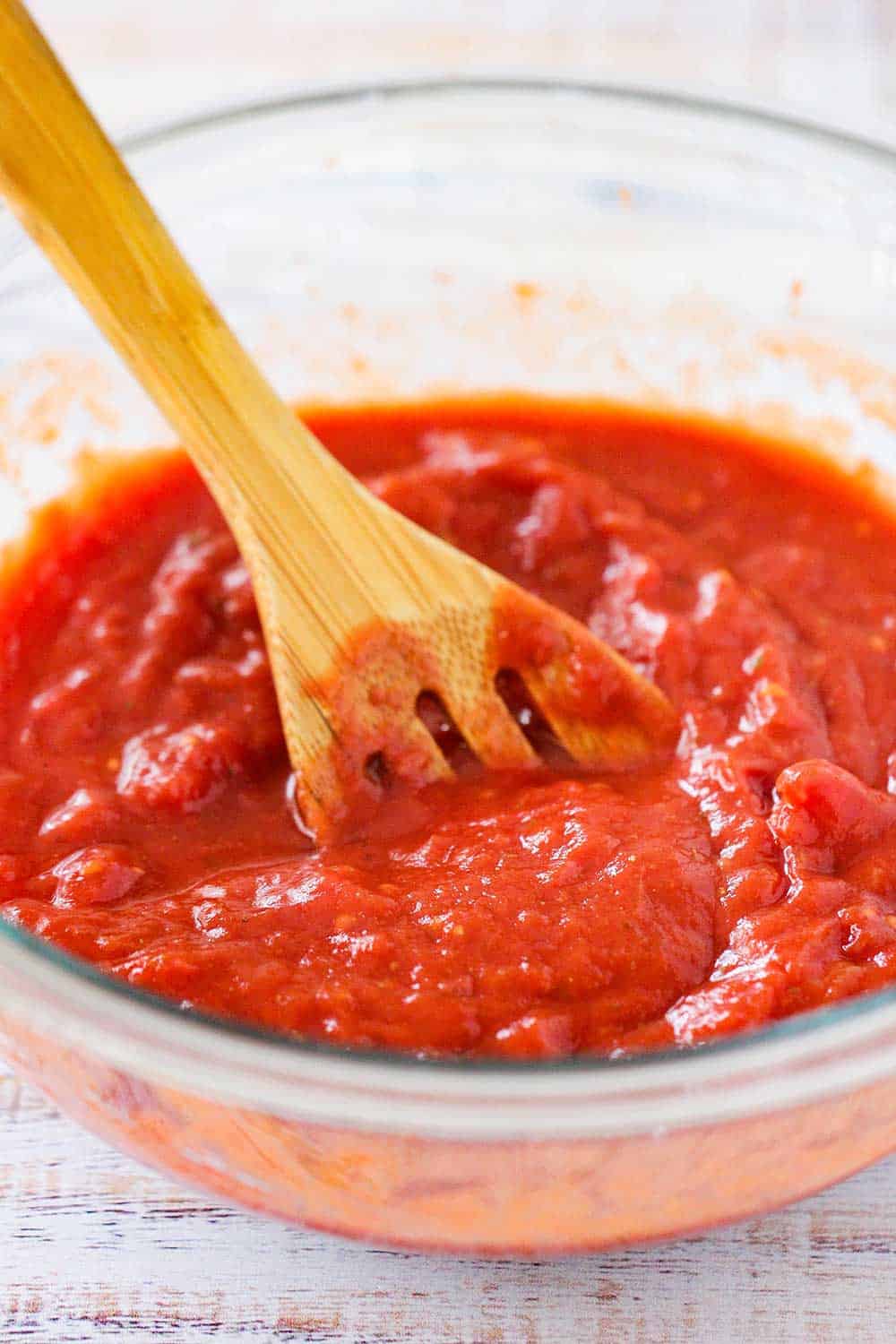 A clear bowl of Chicago deep dish pizza sauce with a wooden spoon in it. 