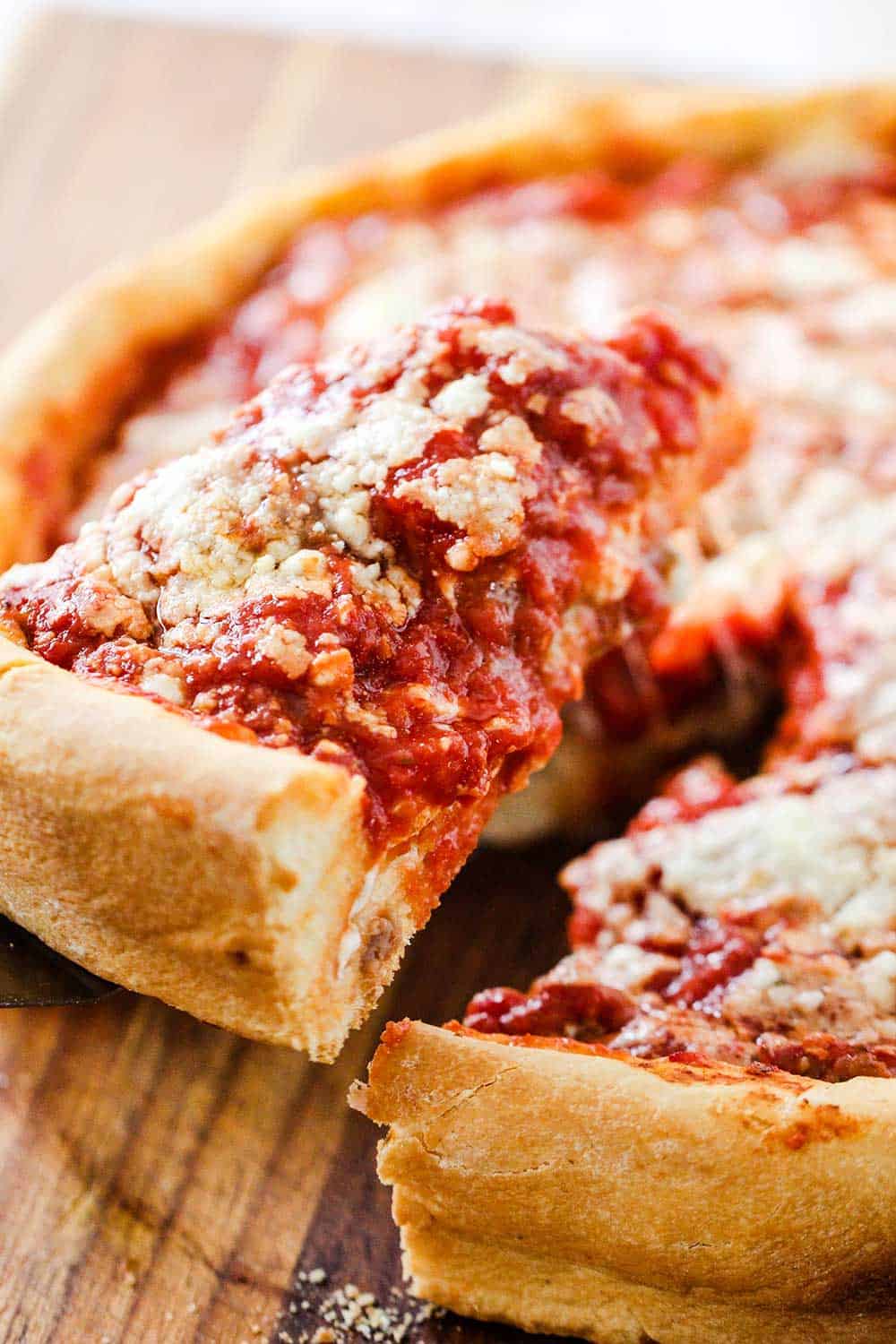A slice of Chicago-style deep dish pizza being lifted from the pizza. 