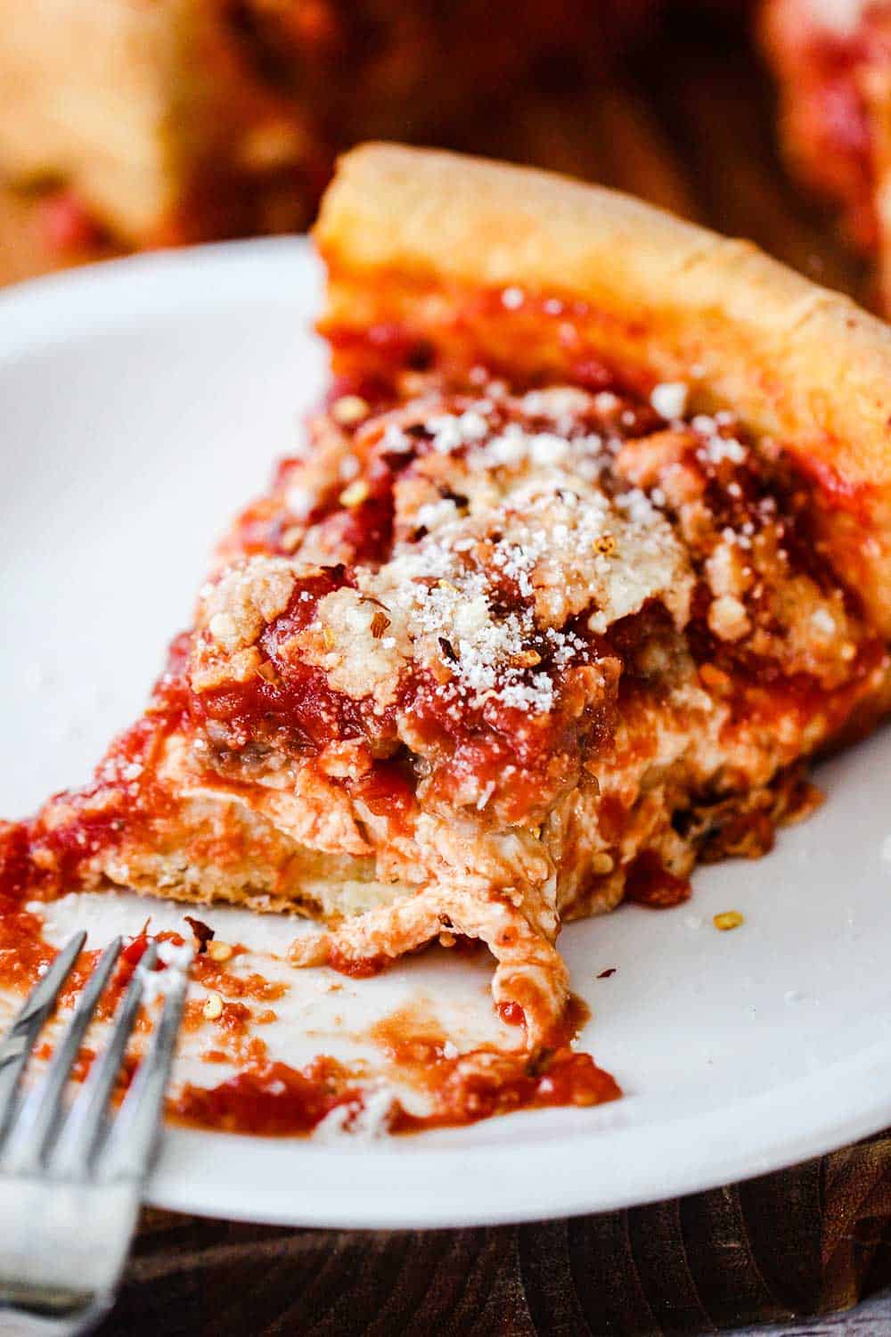 A slice of Chicago-style deep dish pizza on an individual plate with a bite taken out. 