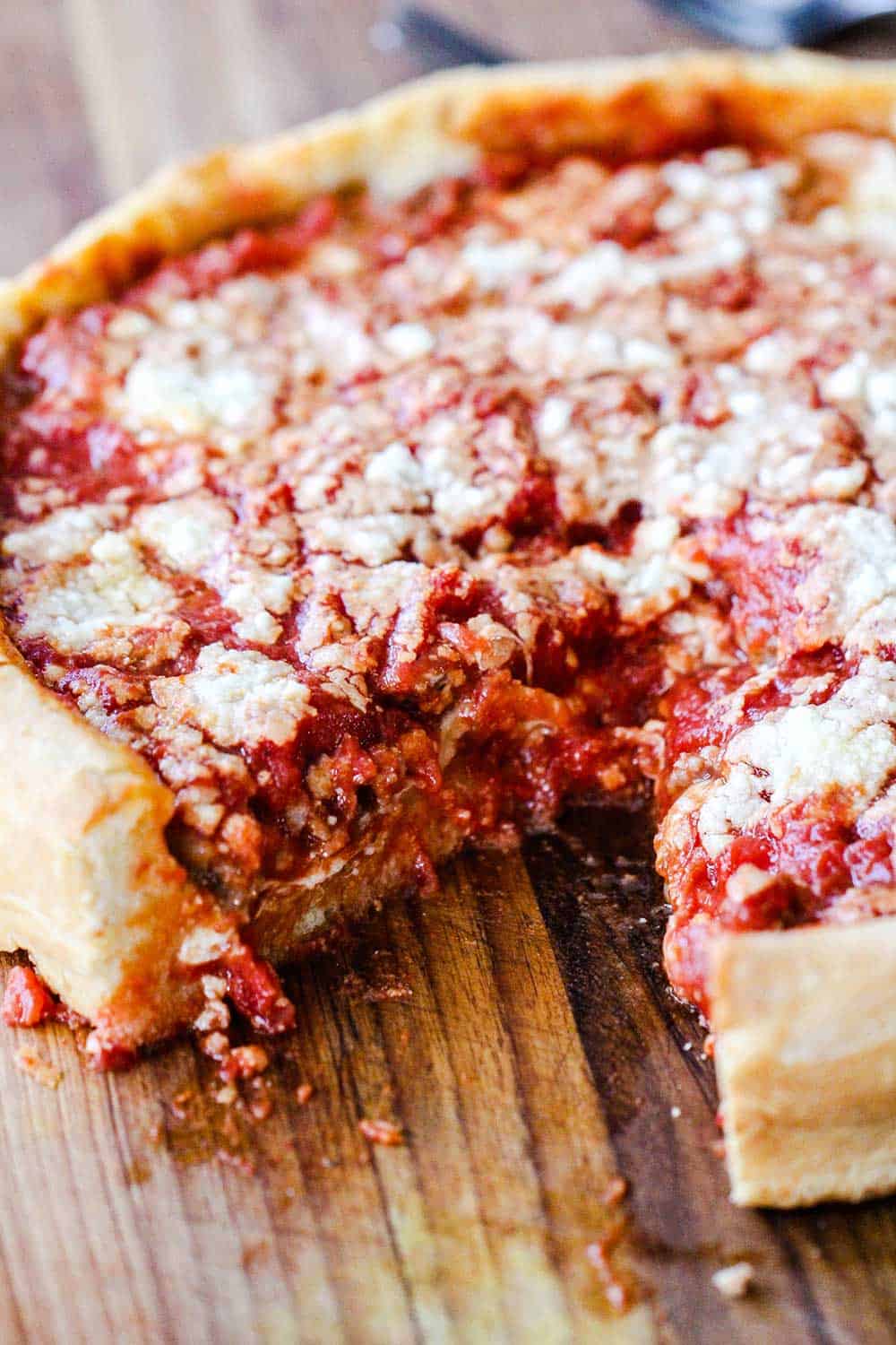 A deep dish pizza with a slice missing on a cutting board. 