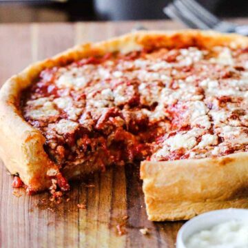 A Chicago-style deep dish pizza with a slice missing sitting on a wooden cutting board.