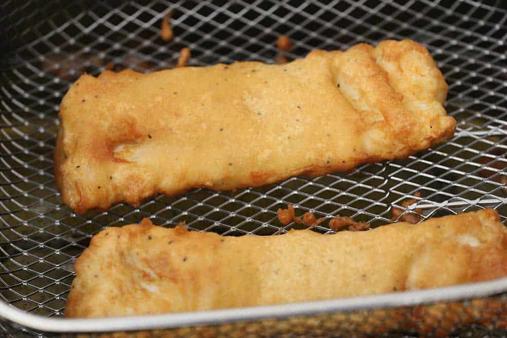 Two fried pieces of cod in a fryer basket. 