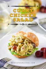 A close-up view of curry chicken salad between two croissant halves on a white plate.