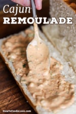 A person transferring Cajun remoulade from a large silver spoon onto the lower half of an open French roll.