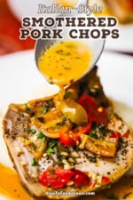 A straight-on view of a large spoon transferring a savory brown sauce over the top of a seared pork chop that is covered with Italian peppers, garlic, and herbs.