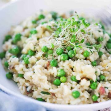A white individual bowl filled with risi e bisi and topped with pea shoots.