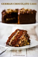 A slice of German chocolate cake on a white dessert plate in front of a cake stand with the cake on it.