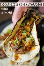 A person holding a Korean beef taco with kimchi in his hand revealing the meat and BBQ sauce on top.