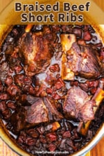 An overhead view of a large oval Dutch oven that is filled with braised beef short ribs in an Italian tomato and vegetable sauce.