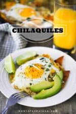 A white plate of chilaquiles topped with a fried egg next to a glass of orange juice.