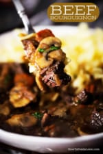 A fork being held up holding a piece of beef and noodles from a bowl of beef bourguignon.