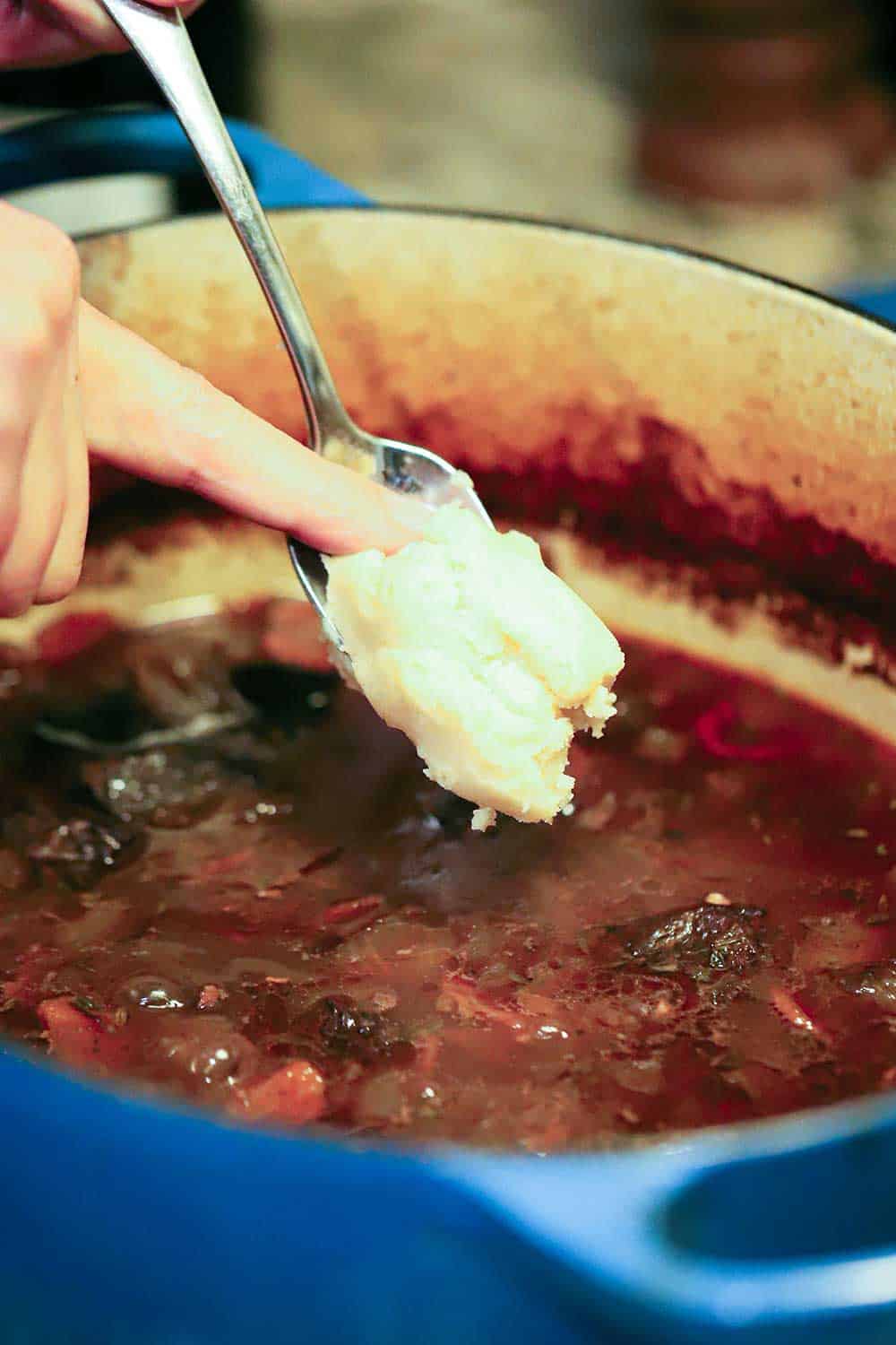 A person using his finger to transfer buerre manie into a pot of beef beef bourguignon. 