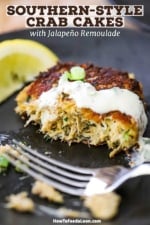 A close-up view of a crab cake topped with a jalapeño remoulade and has been half eaten.