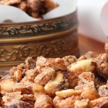 Naughty and Nice Spiced Nuts on a wood cutting board next to a tin with nuts