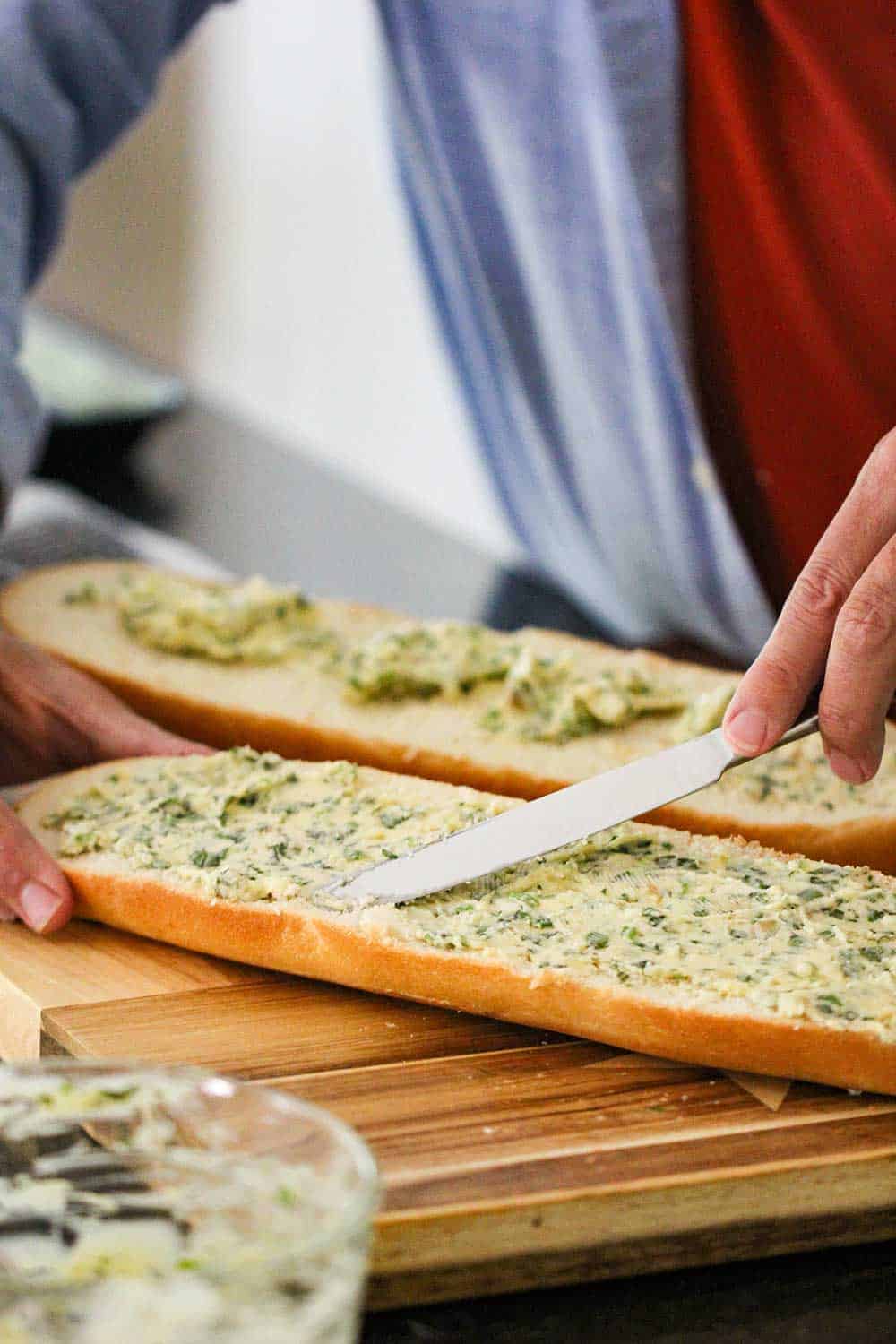 A cook using a knife to smear a butter and garlic mixture over two slices of bread. 