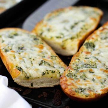 Sliced cheesy garlic bread on a baking sheet.