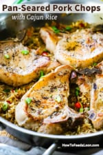 A straight-on view of a large stainless steel skillet filled with pan-seared pork chops on top of seasoned rice.
