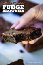 A hand holding a fudge brownie with a bite taken out of it.