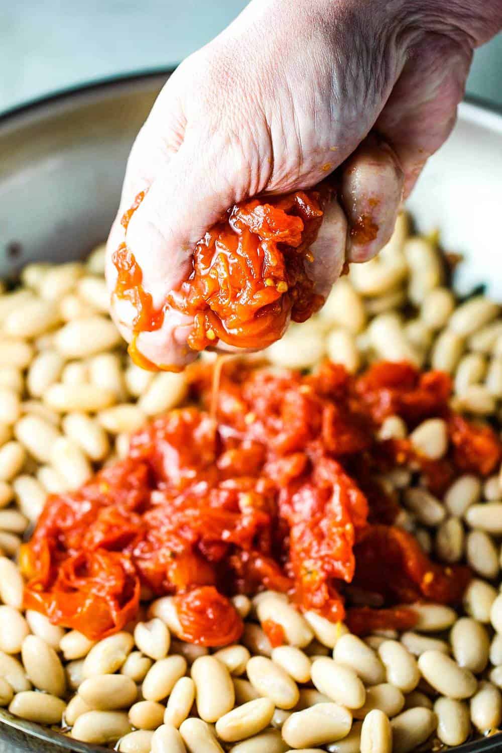 San Marzano tomatoes being hand squeezed into sautéed white beans with sage and garlic