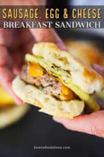 Two hands holding a sausage, egg, and cheese breakfast sandwich with a bite taken out it.