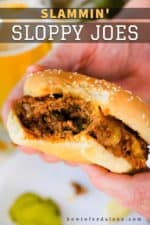 Two hands holding a sloppy joe sandwich with a bite taken out of it.