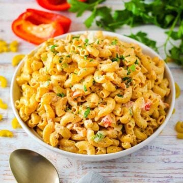 A large white bowl of Cajun Pasta Salad with a gold spoon nearby.