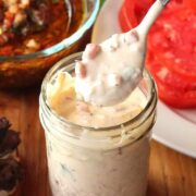 A jar of Chimichurri Mayonnaise sitting next to a plate of slice tomatoes.