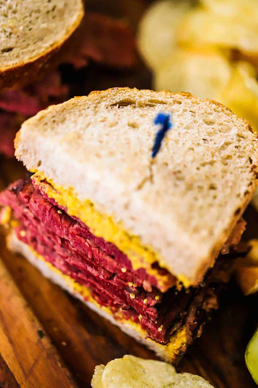 A Wagyu pastrami sandwich sitting on a small cutting board with a toothpick stuck through the middle of it. 
