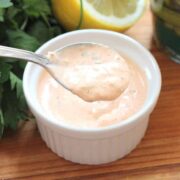 A spoon filled with Homemade Russian Dressing over a small ramekin full of the same next to a lemon half and parsley.