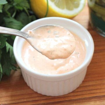 A spoon filled with Homemade Russian Dressing over a small ramekin full of the same next to a lemon half and parsley.