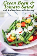 Scallion Buttermilk dressing being poured from a glass container over a green bean and tomato salad on a white platter.