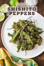 An overhead view of a white serving plate filled with a pile of seared shishito peppers all next to a couple of limes and a small jar of sea salt.