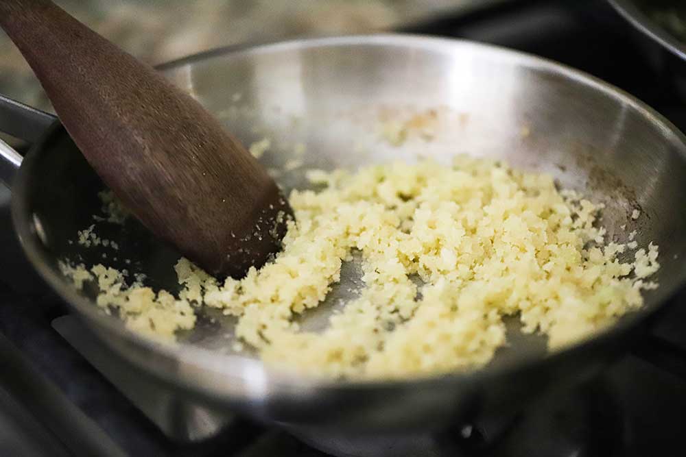 A small silver skillet filled with Panko bread crumbs being stirred into melted butter with a wooden spoon. 