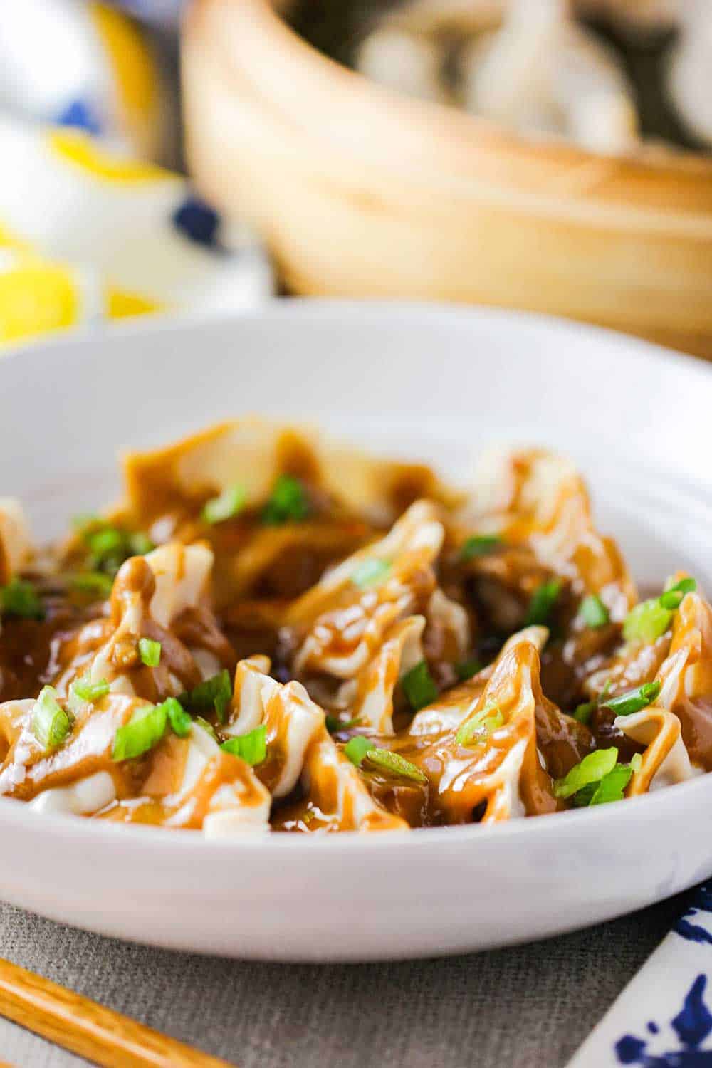 A white bowl of pork dumplings with spicy peanut sauce. 