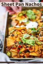 A person pulling a chili cheese nacho from a sheet pan filled with them.