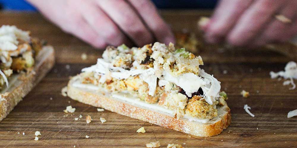 Two hands adding a final layer of dressing onto a Thanksgiving panini. 