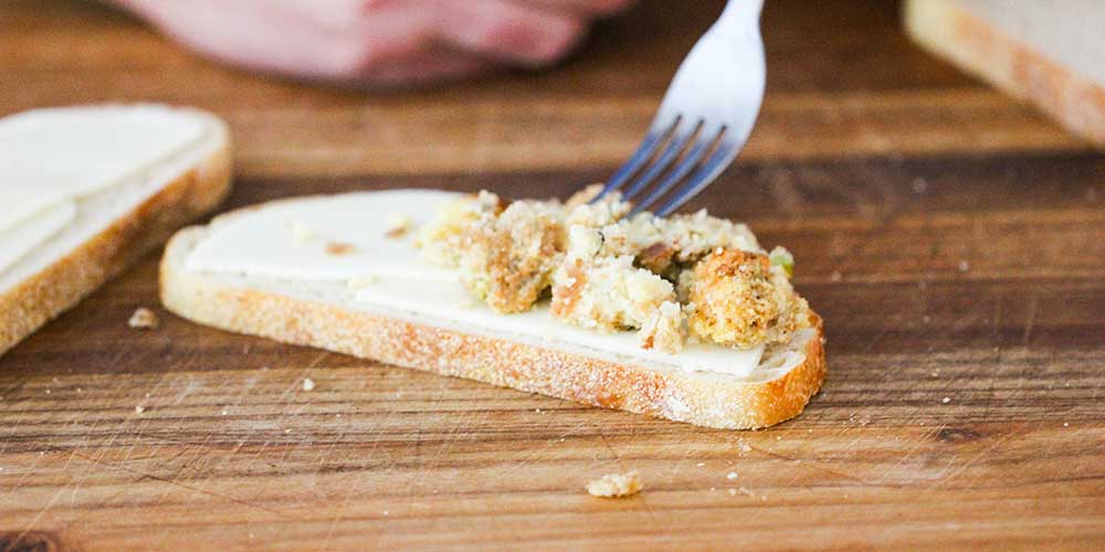 A fork placing dressing onto a slice of bread. 