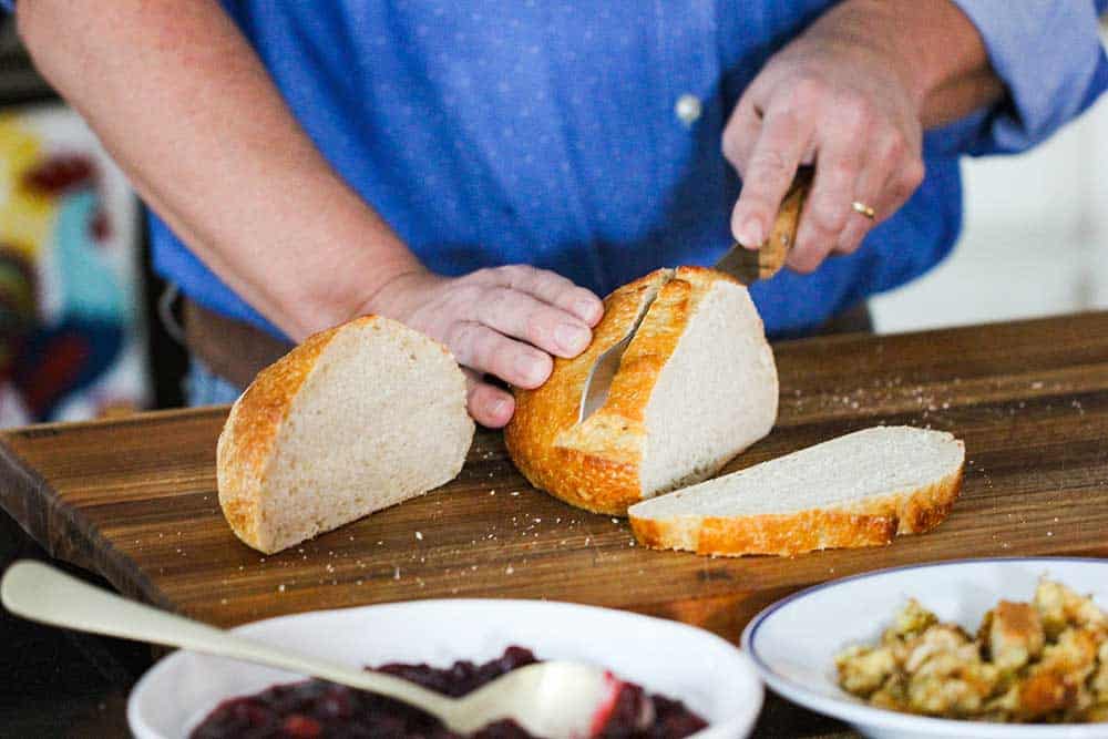 Two hands slicing a loaf of sourdough bread. 