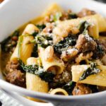 A close-up view of a white bowl holding country Italian pasta with sliced bread next to it.