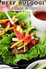 A person using a small spoon to drizzle Korean barbecue sauce over strips of bulgogi beef nestled into a lettuce leaf and toped with julienned carrots and cucumber.