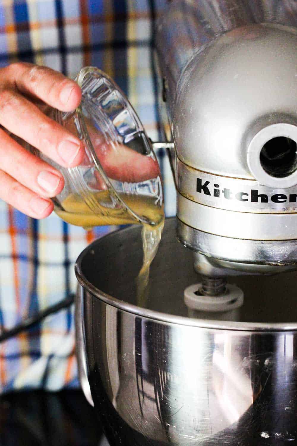 A hand pouring two eggs yolks in a glass bowl into a stand mixer. 