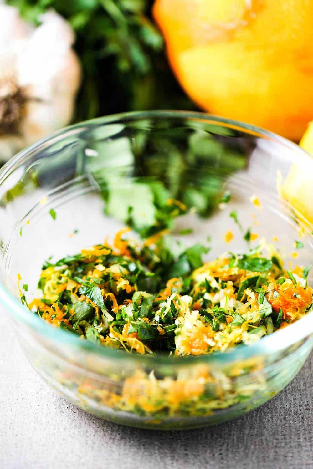 A glass bowl holding a citrus and garlic gremolita